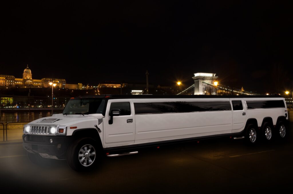 White Hummer limousine on a night tour in Budapest with Chain Bridge and Buda Castle in the background, ideal for stag do parties