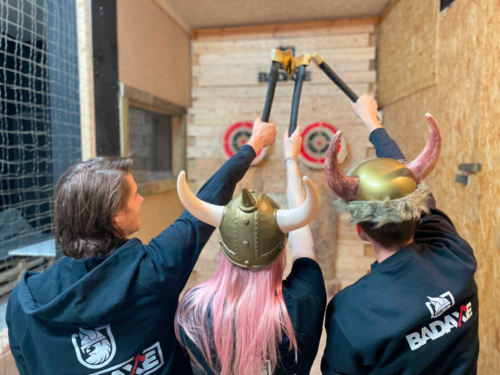 three people celebrating and raising axes while standing at the axe-throwing track