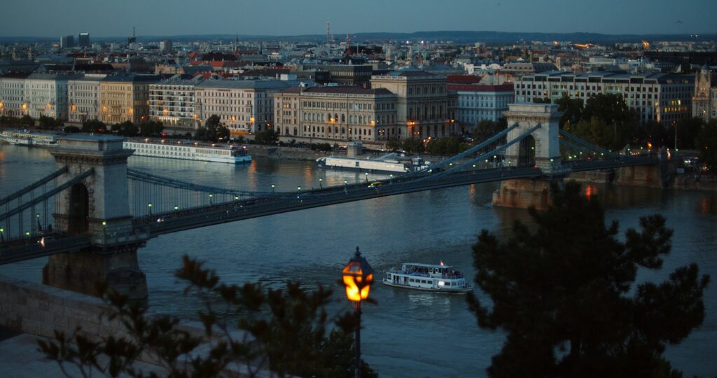 Evening view of the Chain Bridge in Budapest with boats cruising along the Danube River, capturing the city's vibrant nightlife atmosphere.