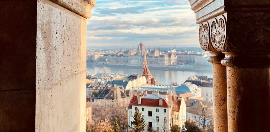 Panoramic view of the Budapest Parliament Building and Danube River framed by historic architecture.