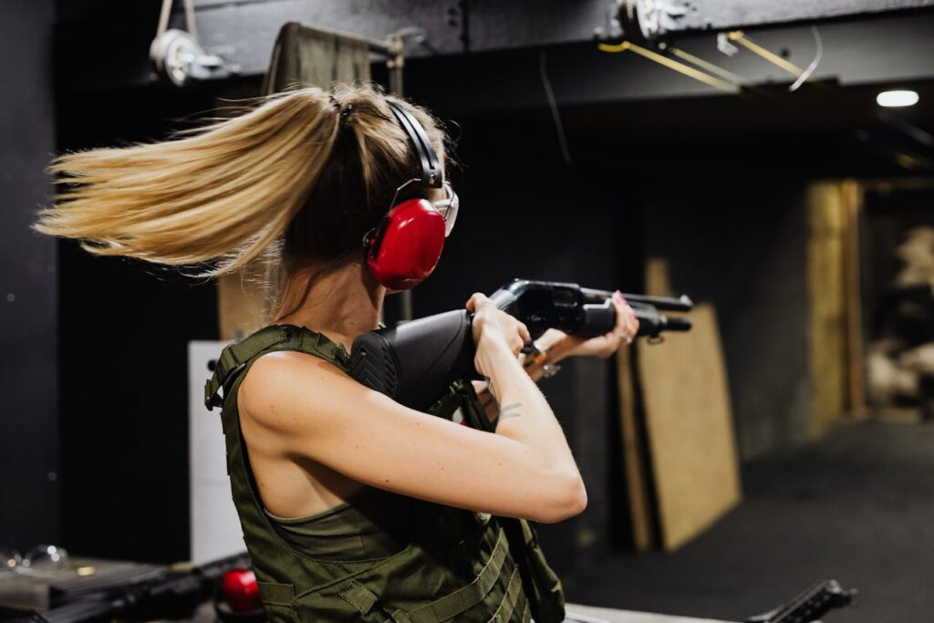 Woman participating in a gun shooting Budapest stag event, aiming a shotgun at an indoor shooting range.