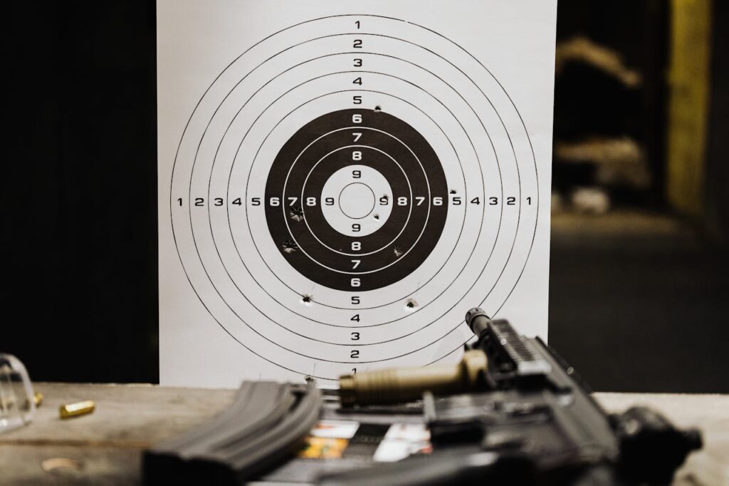 Close-up of a target with bullet holes after a shooting session at an indoor range, with a rifle in the foreground.