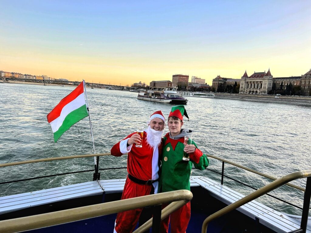 Festive private riverboat party on the Danube in Budapest, featuring Santa and an elf celebrating with Hungarian pride at sunset.