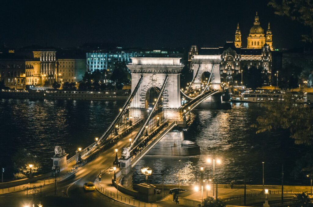 Nighttime view of the iconic Chain Bridge in Budapest, beautifully lit with the Danube River glistening below and St. Stephen’s Basilica in the background.