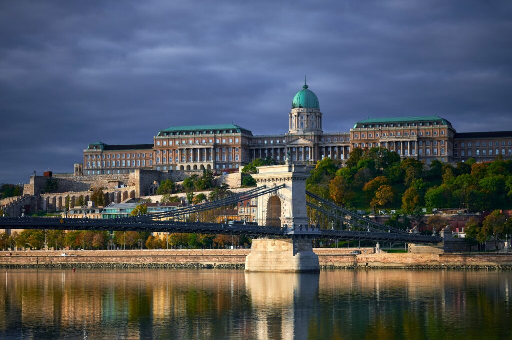 Daytime view of Buda Castle and the Chain Bridge reflecting on the calm waters of the Danube River, a perfect backdrop for private riverboat celebrations in Budapest.