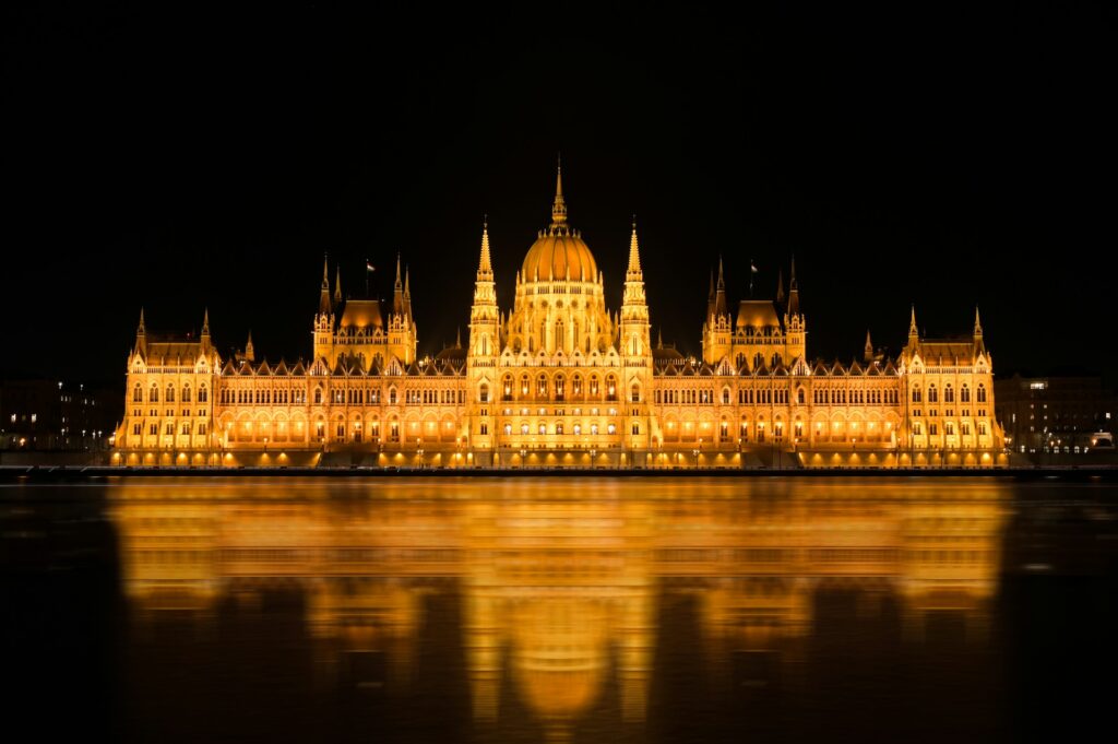 Night view of the Hungarian Parliament building illuminated in golden lights, reflecting perfectly on the calm waters of the Danube River.