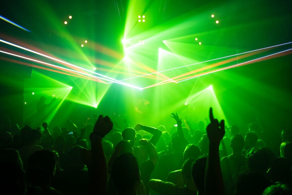 Epic Budapest stag adventures with a vibrant club party, green laser lights, an energetic crowd, and hands raised in celebration on a packed dance floor.