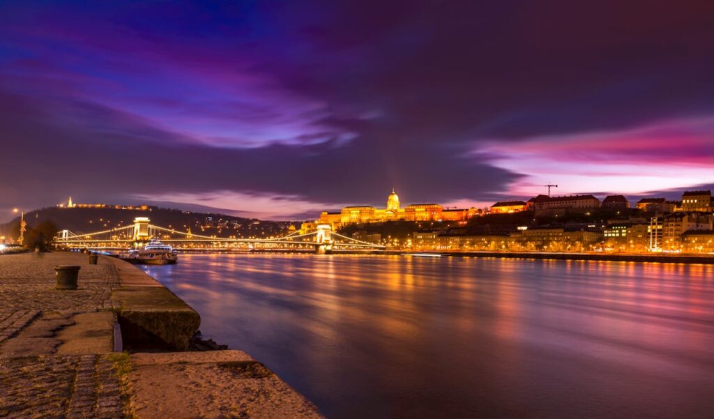  Night view of Budapest with illuminated Chain Bridge, Buda Castle, and colorful sky reflecting on the Danube River, perfect for a stag night atmosphere.