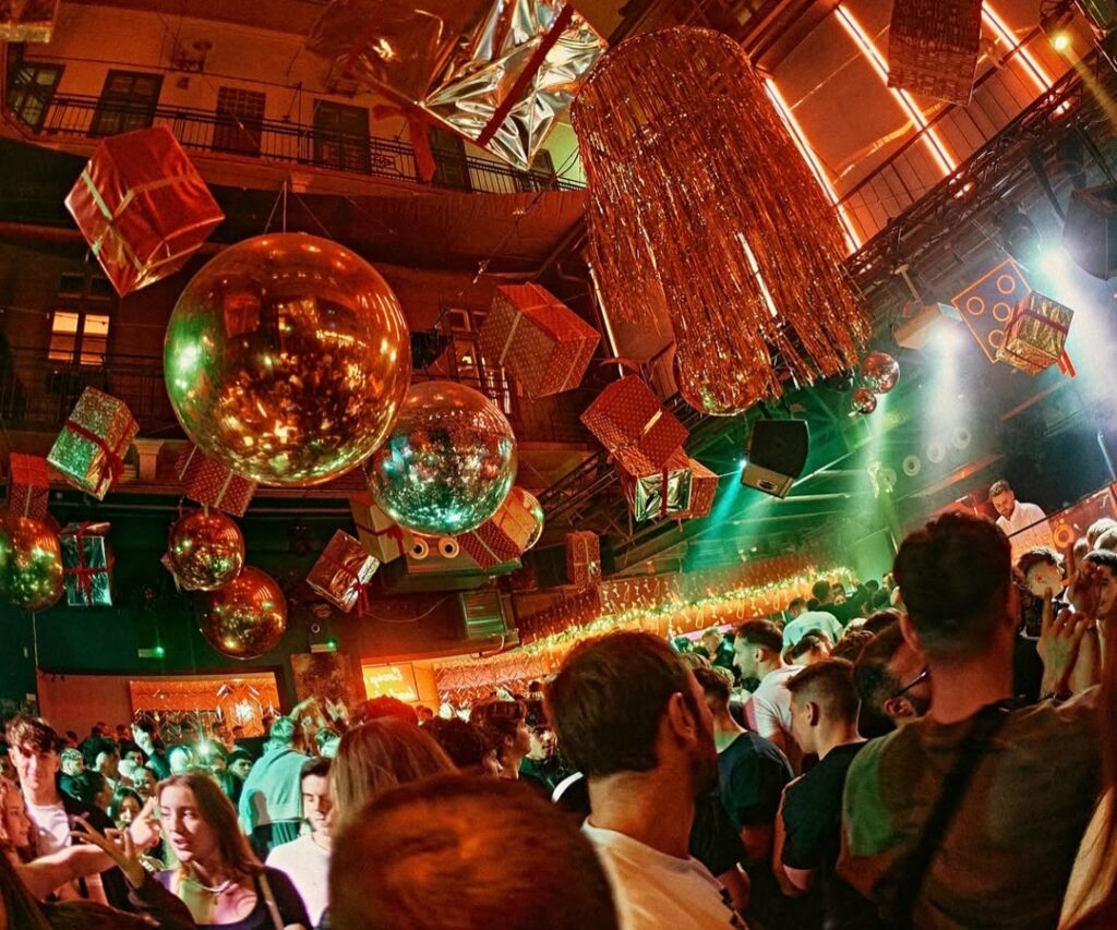 A festive nightclub in Budapest with golden disco balls, shiny decorations, and a lively crowd enjoying the party atmosphere.