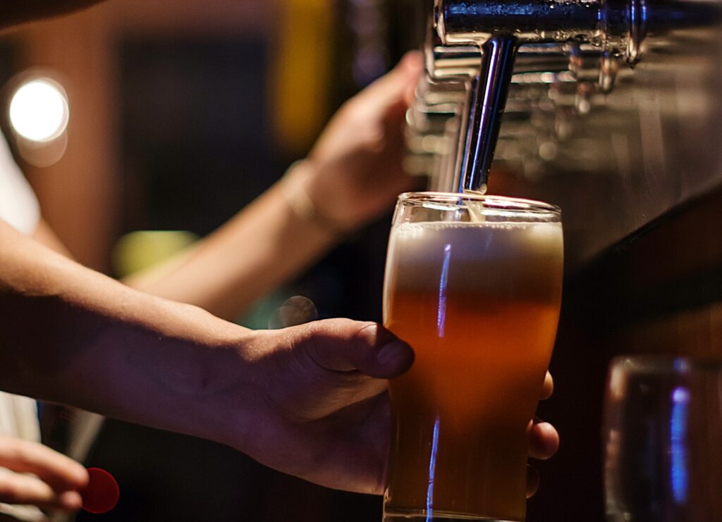 A bartender pours a fresh draft beer into a glass at a dimly lit bar, creating a warm and inviting atmosphere for beer lovers.