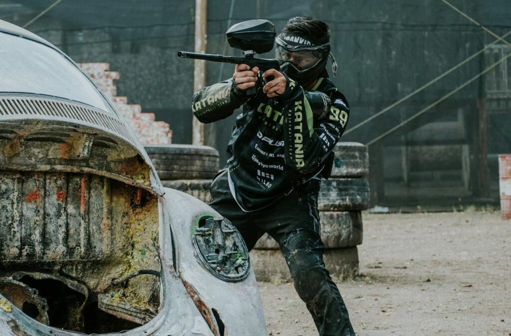 A paintball player in action, wearing protective gear and aiming behind a weathered vehicle, perfect for stag party packages Budapest.