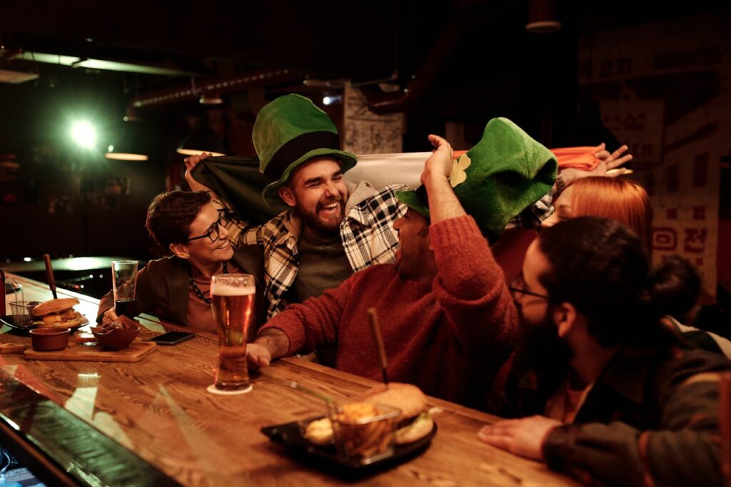 A group of friends laughing and enjoying food and drinks at a cozy pub with festive hats and decorations