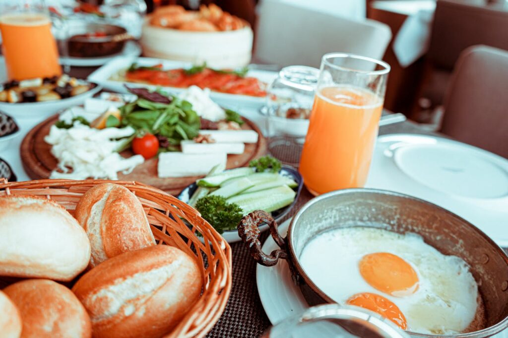 A delicious breakfast spread featuring fresh bread, fried eggs, vegetables, cheese, and a glass of orange juice on a dining table