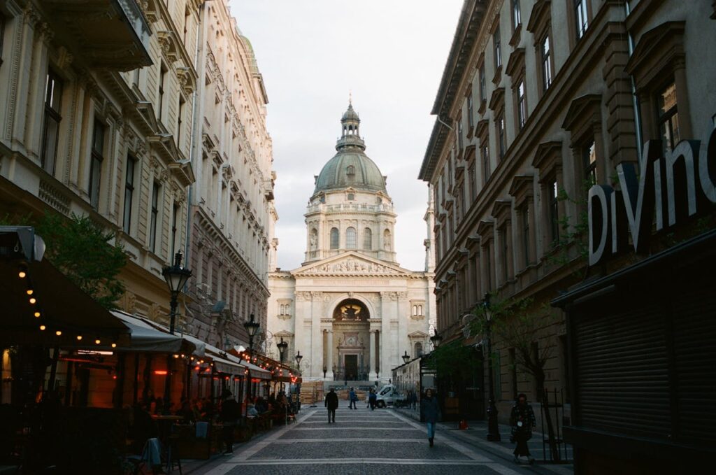 A stunning street view in Budapest, showcasing the iconic St. Stephen’s Basilica, with vibrant bars and terraces, including DiVino Wine Bar, highlighting the city's fantastic nightlife scene.