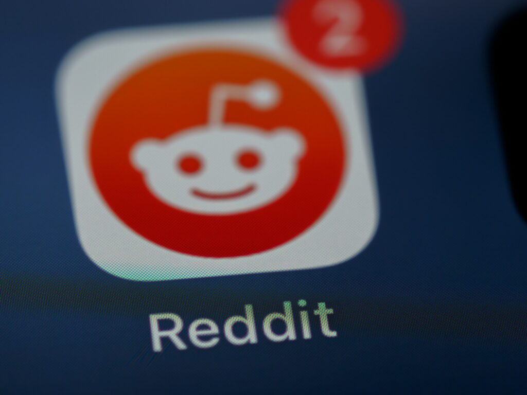 Close-up of the Reddit app icon on a screen, featuring the orange and white alien logo with a red notification badge showing the number two, indicating new alerts or messages, representing Budapest Stag Do Reddit threads.