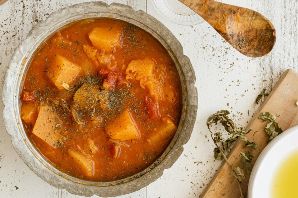 A traditional Hungarian goulash served in a rustic metal bowl, featuring tender chunks of meat, potatoes, and vegetables in a rich, paprika-seasoned broth, garnished with herbs