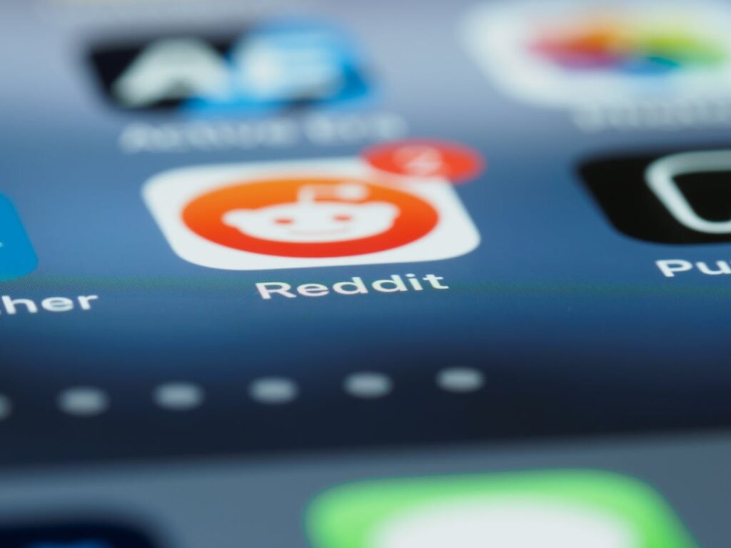 A close-up of a smartphone screen displaying the Reddit app icon with a red notification badge showing four new alerts, alongside other app icons in a blurred background.