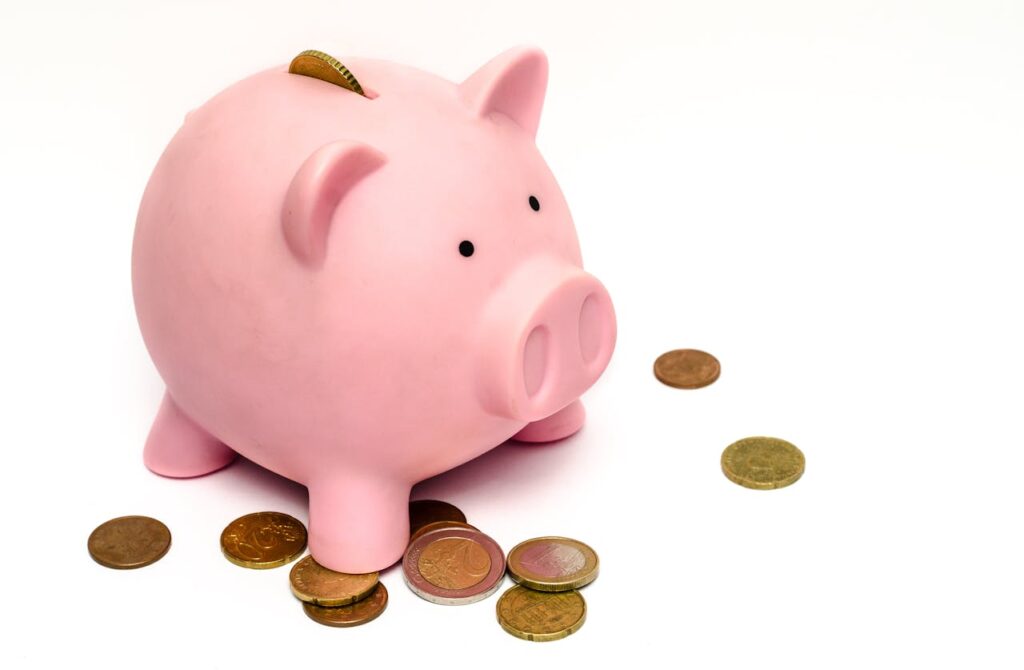 A pink piggy bank with a coin inserted into its slot sits on a white surface, surrounded by scattered coins, symbolizing savings and financial planning.