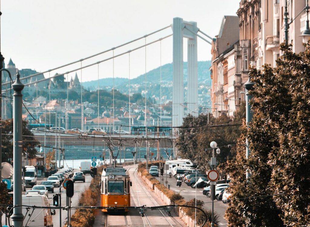 A classic yellow tram travels along the tracks in Budapest, Hungary, with the Elizabeth Bridge and Buda hills in the background, capturing the city's historic and modern charm.